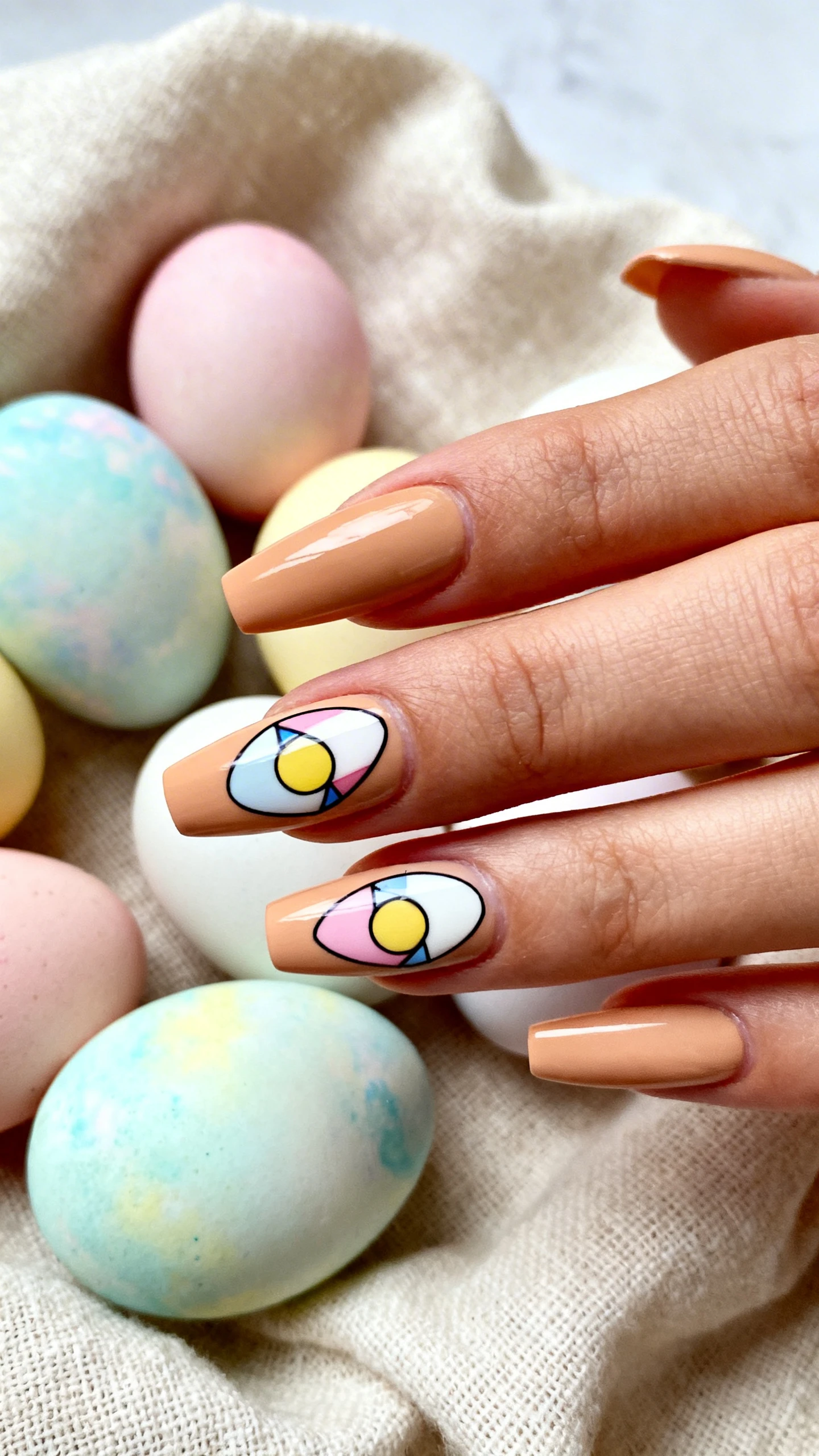 A beautiful macro photograph of one hand showing long, coffin-shaped nails. The base color is a warm beige featuring abstract geometric egg shape stickers in pastel hues. High-resolution, sharp focus on the nails. Aesthetic background of pastel dyed Easter eggs arranged on a linen cloth. Modern, Instagram-worthy photography style. No faces visible, focus ONLY on the nails and hand., macro nail photography, high quality, Instagram-worthy, clean composition