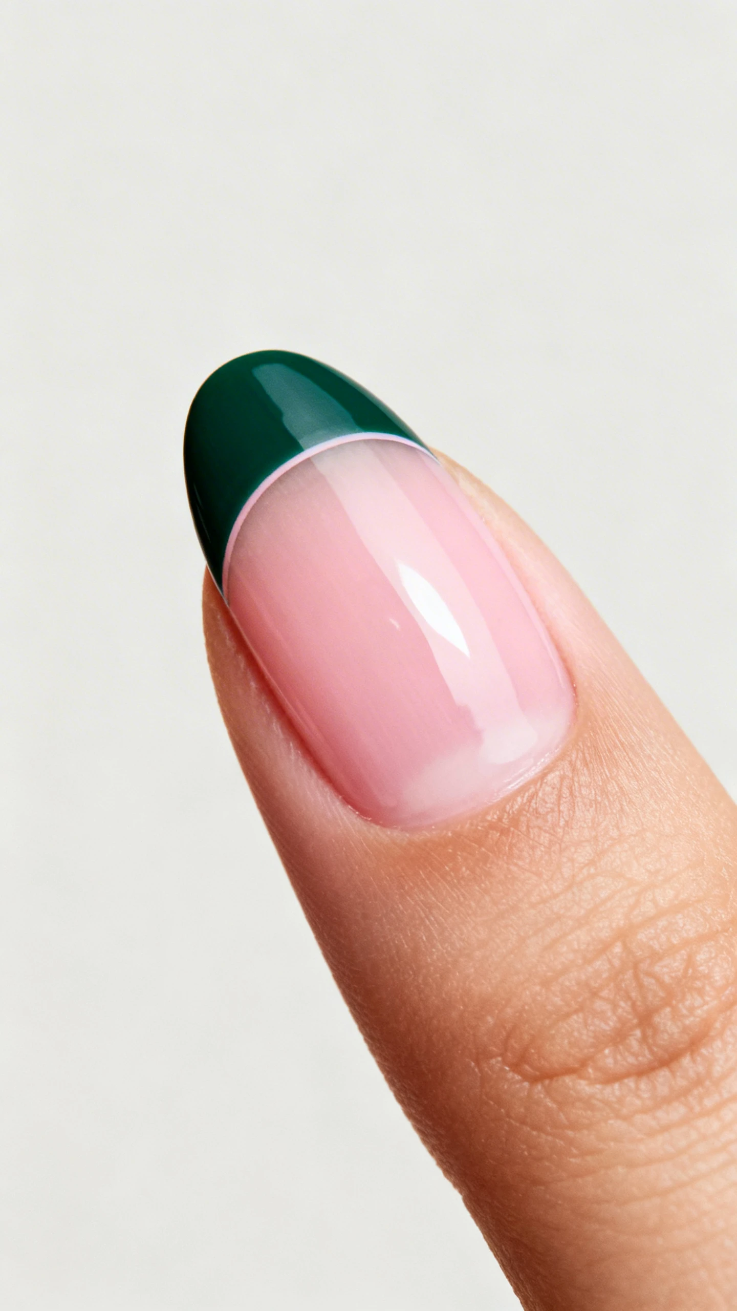 A detailed macro photograph of one hand with medium almond nails, clear-to-very-sheer pink glossy base. A deep forest green micro French sits 1 mm above the free edge, leaving a