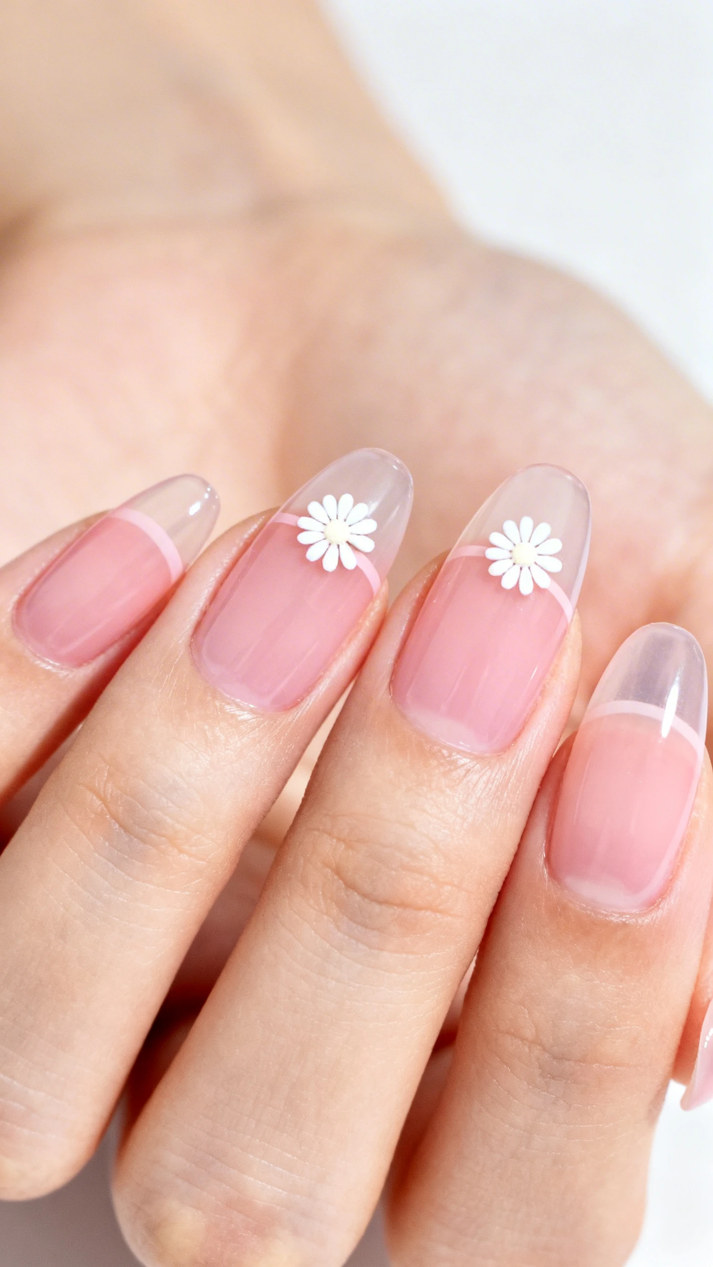 Macro photo of one hand with medium almond nails, sheer ballet-slipper pink base in two thin jelly coats; on ring finger and thumb only, a single micro-daisy each placed at the sidewall midway up the nail: five tiny white petals (