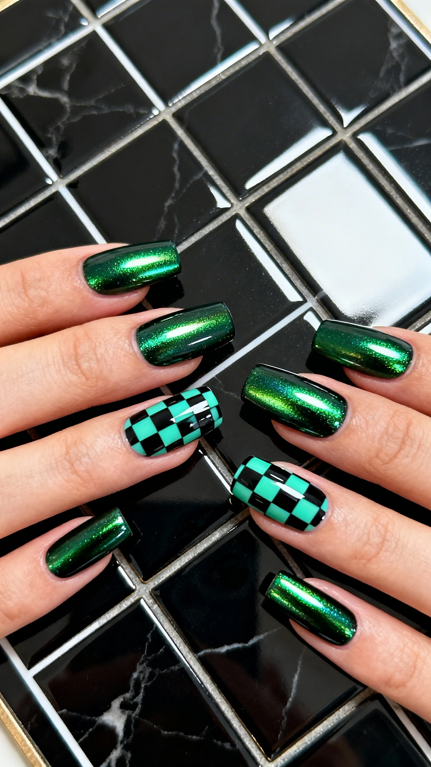 Macro photo of one hand with medium coffin/soft square nails in an Emerald Chrome Checkerboard. Most nails feature deep emerald gel topped with burnished emerald chrome for a mirror-like, reflective green finish. Two accent nails per hand display a crisp black-and-emerald checkerboard pattern, perfectly squared and high-contrast, with glossy top coat. Lighting is bright and controlled to showcase mirror reflections and crisp edges. Background: sleek black marble or glossy ceramic tile evoking a modern board pattern. High-resolution, sharp focus on nails only; no faces.