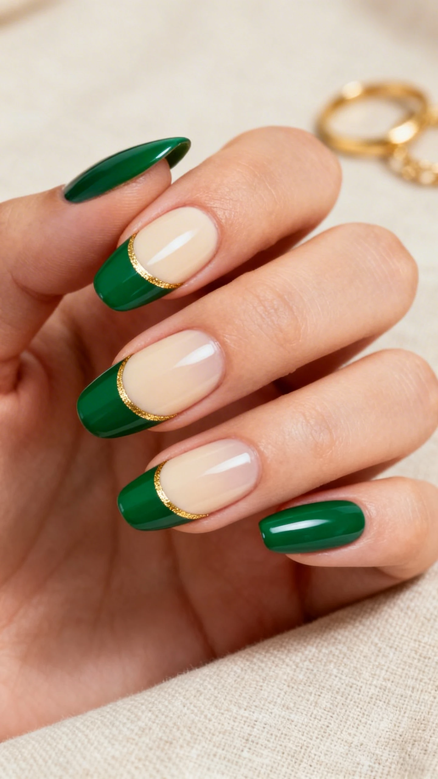 Macro photo of one hand with medium-length almond/squoval nails in a Gilded Emerald French. Base is 1–2 thin coats of sheer cream-beige gel, tips are curved French in deep jewel-toned emerald green with medium thickness and perfectly smooth smile lines. An ultra-fine metallic gold gel liner traces just beneath each green tip as a delicate accent. Lighting is soft and glossy to highlight the shine and crisp lines. Background: luxe neutral linen with a hint of gold jewelry props (rings out of frame blur) for a refined, St. Patrick’s Day vibe. High-resolution, sharp focus on nails only; no faces.