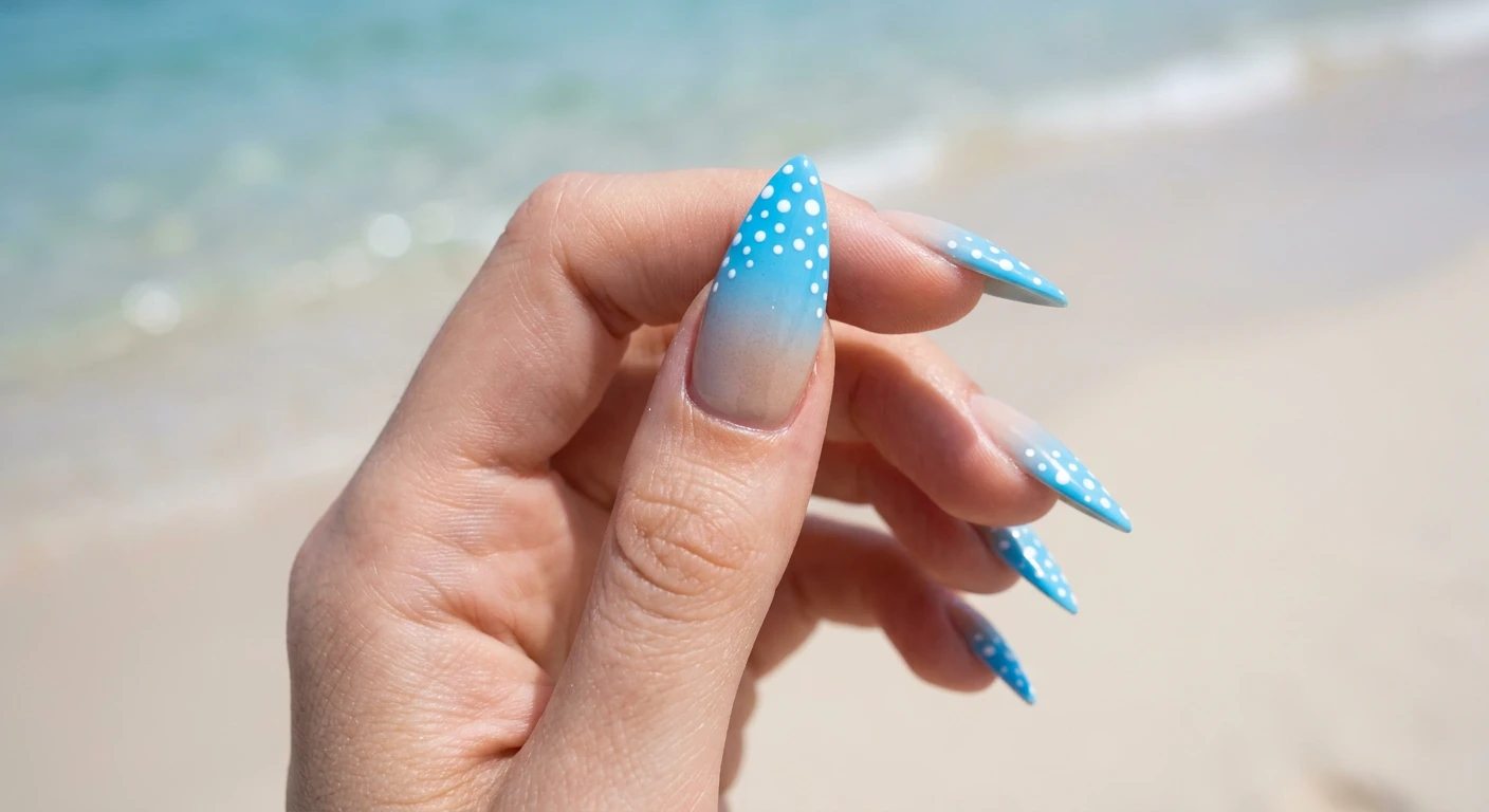 A beautiful macro photograph of one hand showing elegant stiletto-shaped nails in detail, no faces visible. The design is a smooth gradient ombré starting with a soft sand color at the cuticle that fades flawlessly into a bright sky blue at the tip, overlaid with precisely placed, varying small bright white polka dots on the blue tips. High-resolution, sharp focus on the nails. Modern, Instagram-worthy photography style with an aesthetic background of softly blurred pristine fine sand and shimmering light blue water elements., macro nail photography, high quality, Instagram-worthy, clean composition