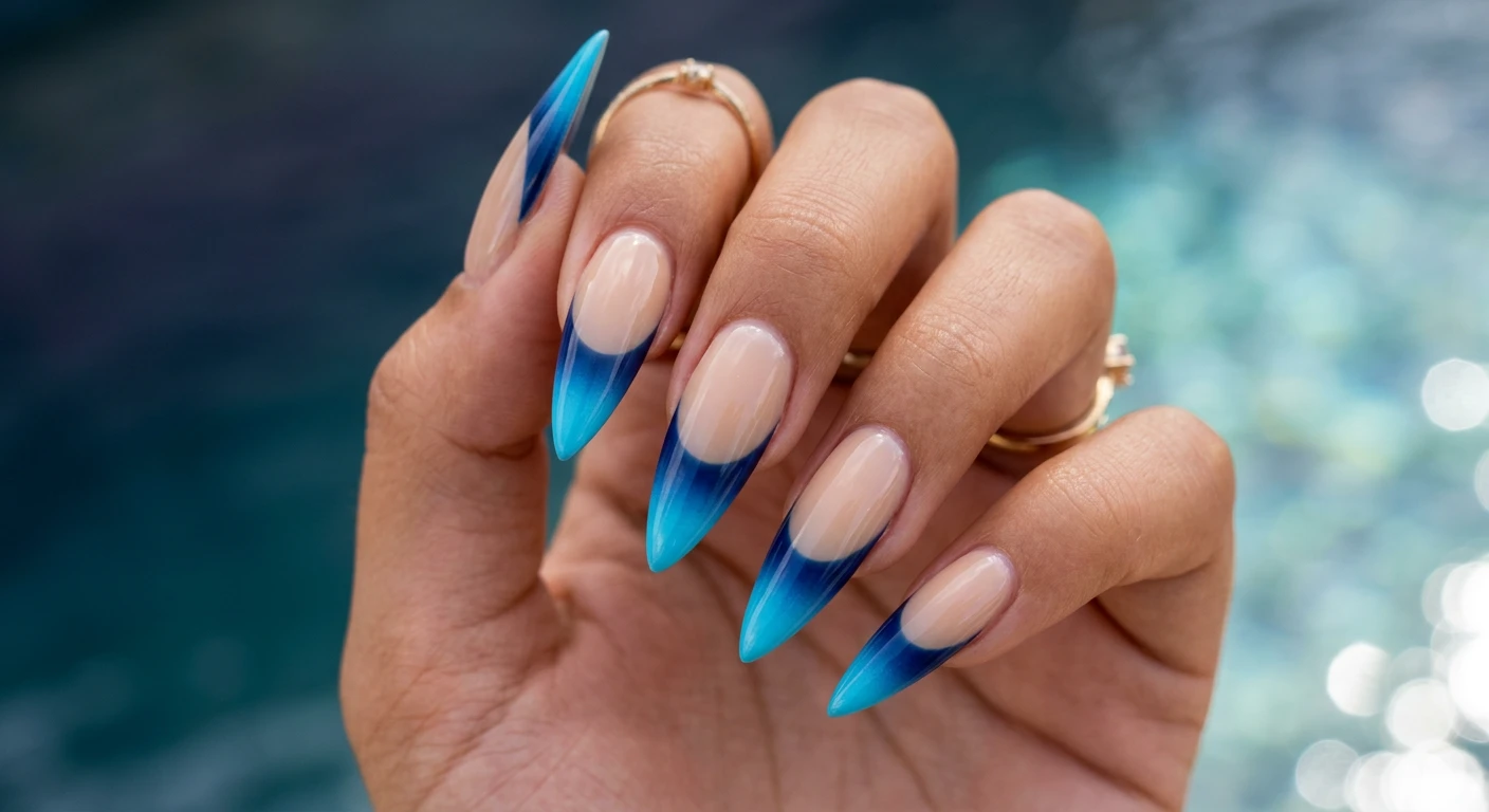 A beautiful macro photograph of one hand showing long stiletto shape nails in detail. The design features a sheer beige base color across the nail bed and thick French tips with a seamless ombré fade starting from deep navy blue at the smile line and transitioning to bright cyan at the very edge, completed with a glossy finish. High-resolution, sharp focus on the nails. Aesthetic background featuring a gradient of deep twilight ocean water transitioning into bright surface reflections. Modern, Instagram-worthy photography style. No faces visible, focus ONLY on the nails and hand., macro nail photography, high quality, Instagram-worthy, clean composition